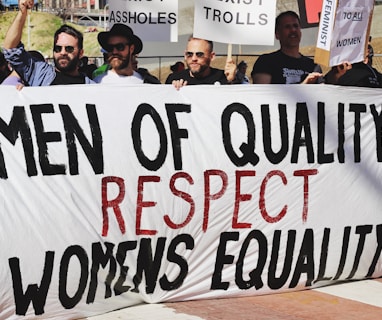 men holding white, black, and red Men of quality respect womens equality banner on road