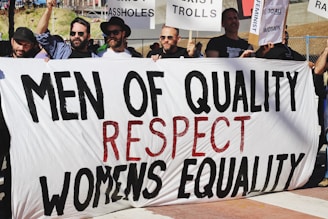 men holding white, black, and red Men of quality respect womens equality banner on road