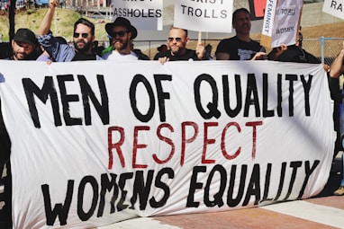 men holding white, black, and red Men of quality respect womens equality banner on road