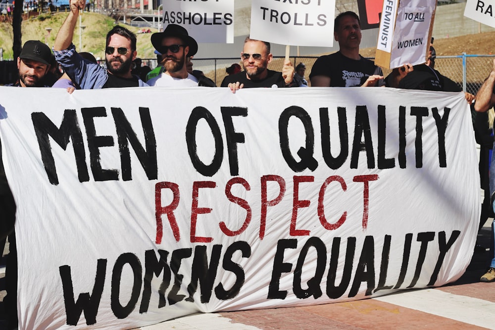 men holding white, black, and red Men of quality respect womens equality banner on road