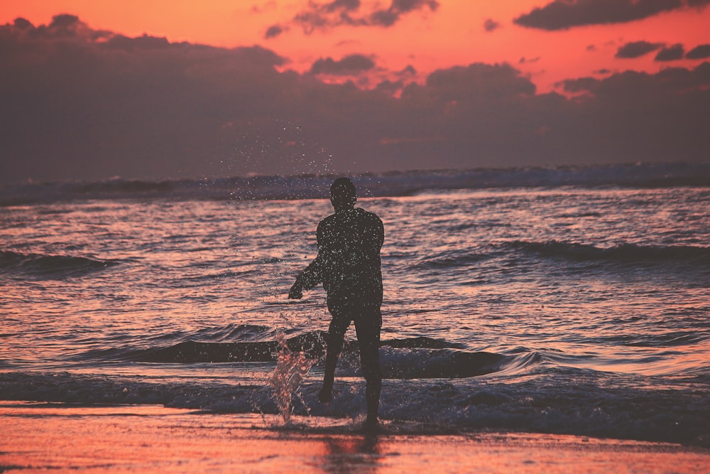 silhouette of person on sea shore during golden hour