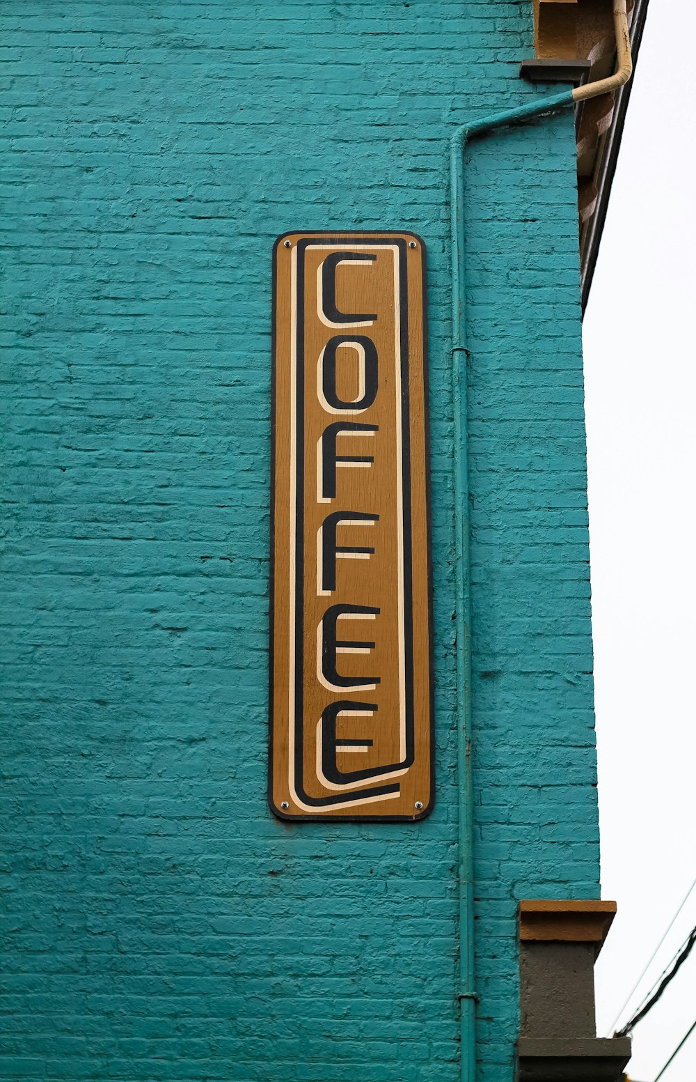 panneau de café en bois marron et noir sur mur de briques bleues pendant la journée