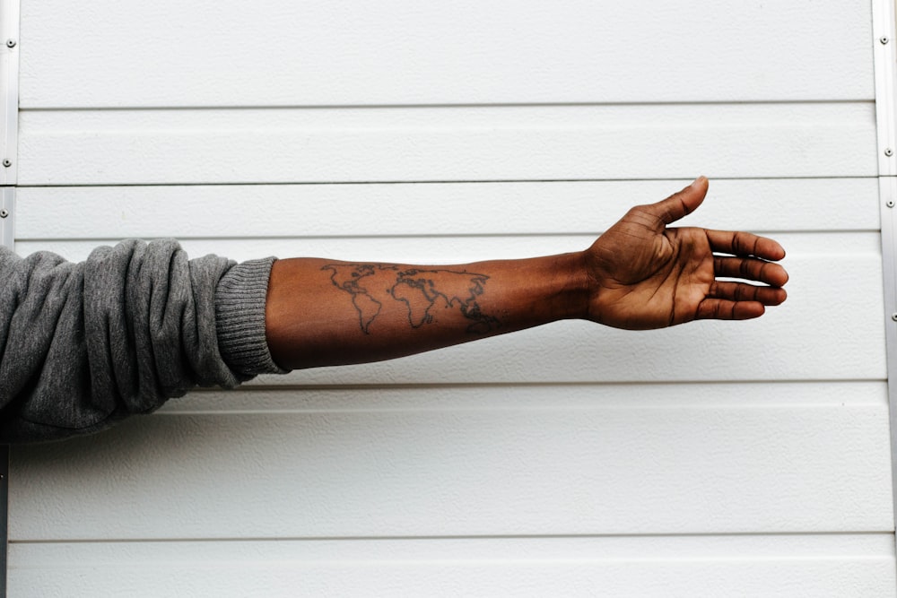 man raising hand with map arm tattoo behind white painted wall