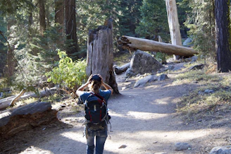 A person hiking on a sunny trail, carrying a backpack with tdm sunshine lotion visible in the side pocket.