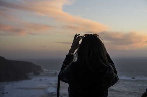 A traveler standing on a cliff overlooking the ocean at sunset.