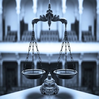 An ornate balance scale with intricate detailing is prominently positioned in the foreground against a blurred architectural backdrop of arches and columns, conveying a sense of elegance and precision.