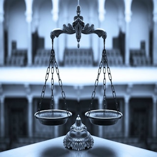 An ornate balance scale with intricate detailing is prominently positioned in the foreground against a blurred architectural backdrop of arches and columns, conveying a sense of elegance and precision.