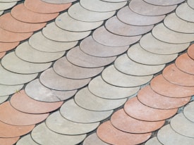 An arrangement of semi-circular tiles in a scale-like pattern, with alternating shades of beige and light terracotta creating a visually interesting surface.