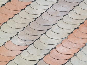 An arrangement of semi-circular tiles in a scale-like pattern, with alternating shades of beige and light terracotta creating a visually interesting surface.
