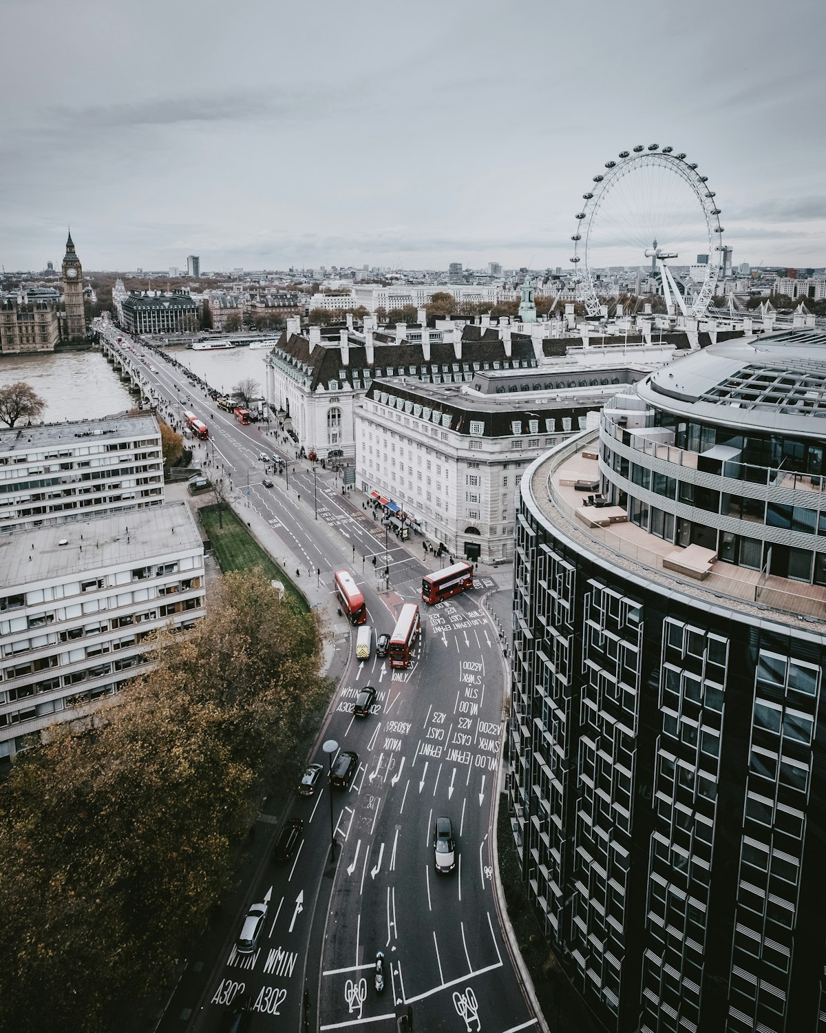 A high view over a busy London road with red buses and traffic, the London Eye in the distance