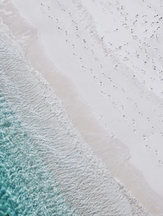 A sunlit beach with turquoise waves and a traveler's footprints in the sand.