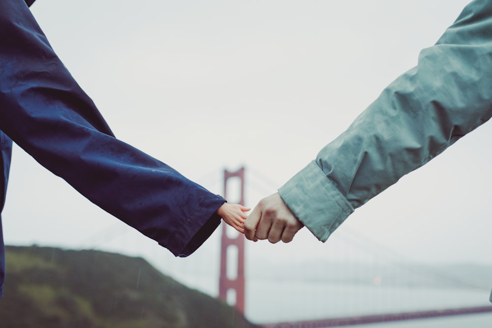 two people holding hands in front of the golden gate bridge