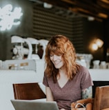 woman sitting on brown wooden chair while using silver laptop computer in room