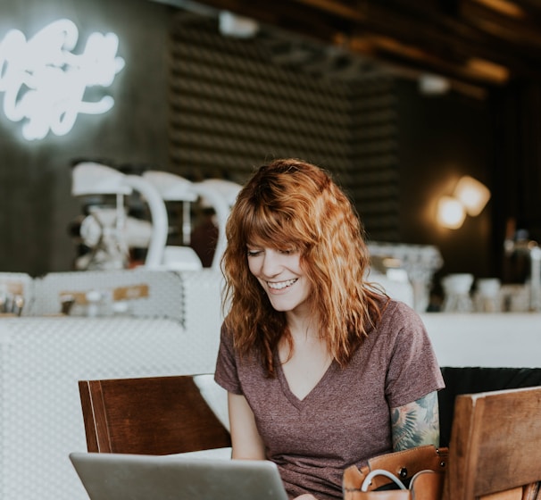 woman sitting on brown wooden chair while using silver laptop computer in room