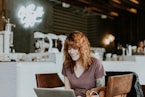 woman sitting on brown wooden chair while using silver laptop computer in room