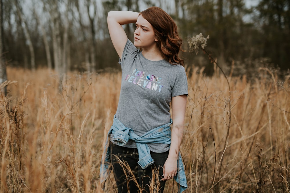 shallow focus photography of woman in gray crew-neck shirt standing in the middle of brown grass field during daytime