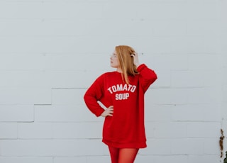 woman wearing red long-sleeved shirt standing near white painted wall