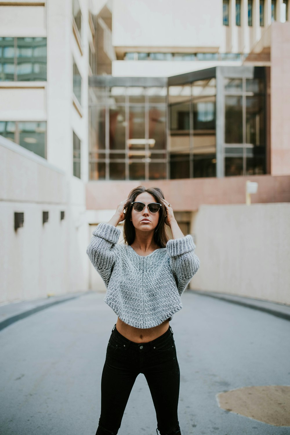 woman in grey knit shirt standing on roadway during daytime