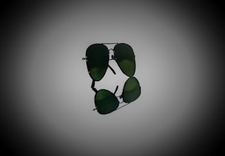 A pair of aviator sunglasses with dark green lenses, prominently displayed against a gradient background. The sunglasses are positioned horizontally, with their reflection visible below.