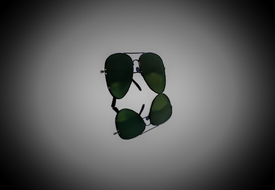 A pair of aviator sunglasses with dark green lenses, prominently displayed against a gradient background. The sunglasses are positioned horizontally, with their reflection visible below.