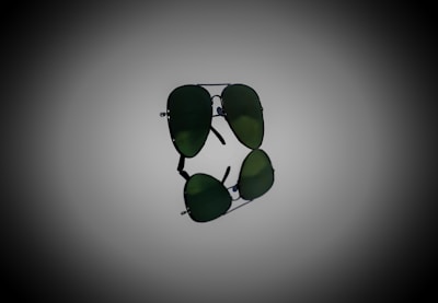 A pair of aviator sunglasses with dark green lenses, prominently displayed against a gradient background. The sunglasses are positioned horizontally, with their reflection visible below.
