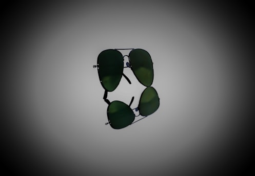 A pair of aviator sunglasses with dark green lenses, prominently displayed against a gradient background. The sunglasses are positioned horizontally, with their reflection visible below.