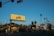 A street scene featuring a prominent yellow billboard with 'Los Feliz' written on it. The image includes various businesses such as 'Tang's Donuts & Ice Cream' and tall palm trees lining the street. Cars drive along the road under a clear blue sky with street signs reading 'Fountain' and 'Sunset'.
