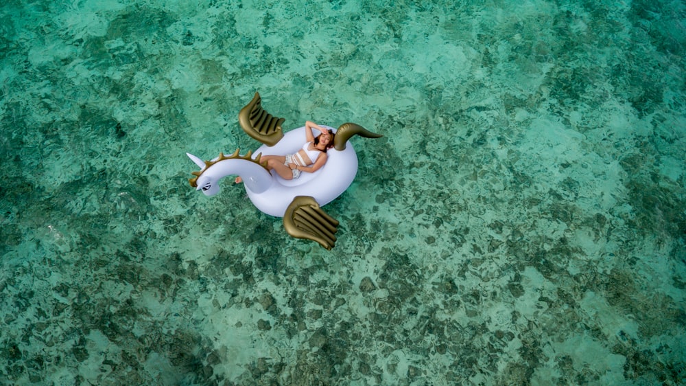 femme portant un ensemble de bikini blanc allongé sur un flotteur gonflable de licorne blanche et marron