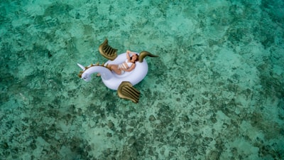 woman wearing white bikini set lying on white and brown unicorn inflatable float summertime google meet background