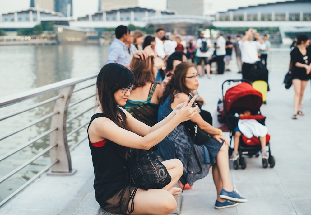 woman wearing black crew-neck sleeveless shirt sitting on floor beside rail while holding gadget