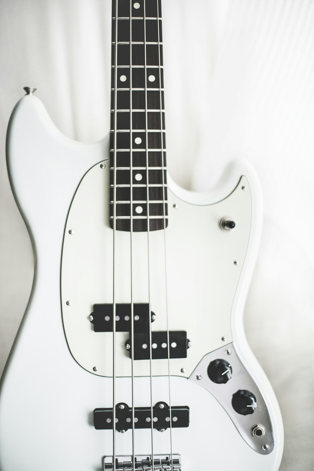 white and black electric bass guitar on white surface