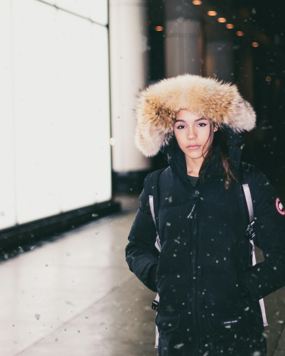 woman in black parka jacket standing while snowing