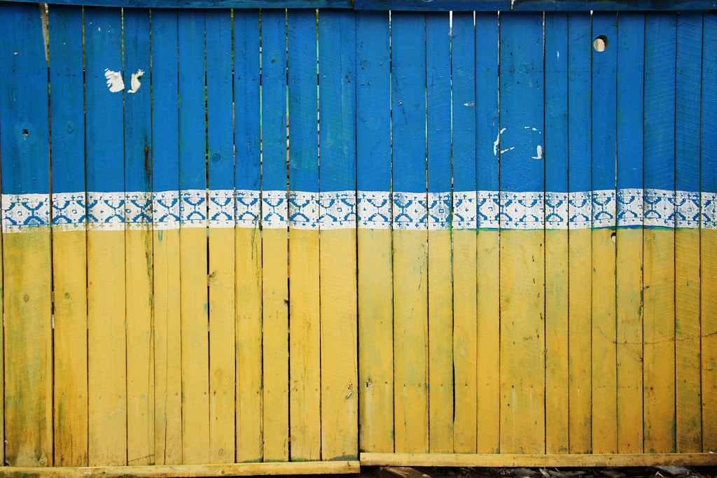yellow and blue wooden fence. Photo by Tina Hartung on Unsplash.