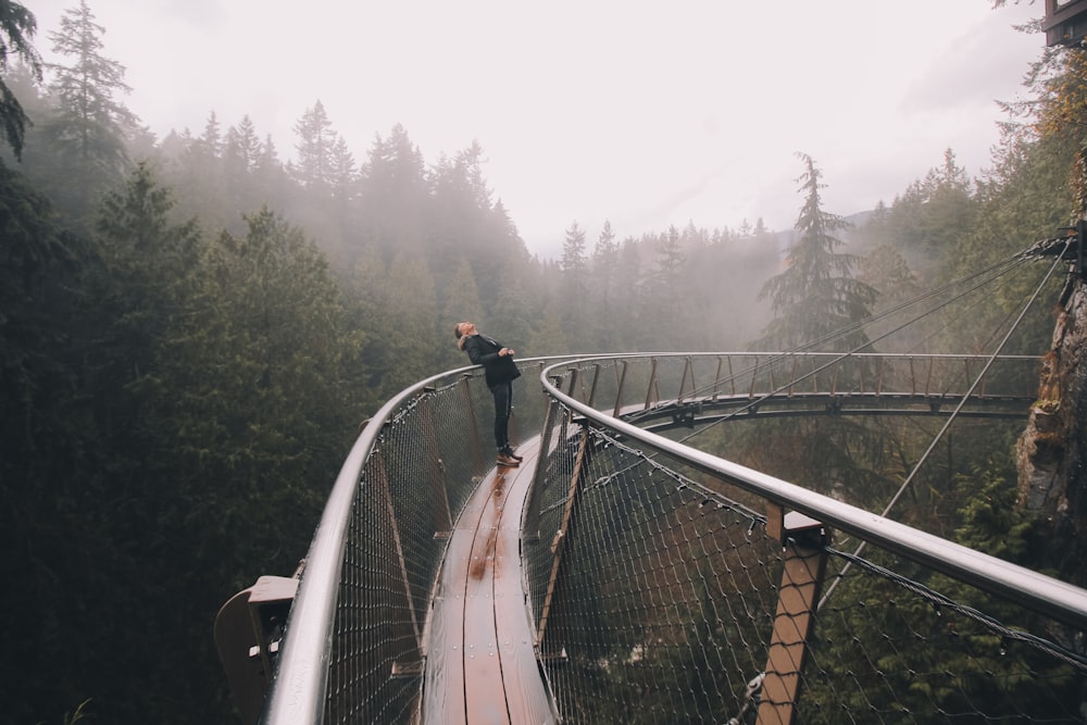 person leaning on bridge beside forest