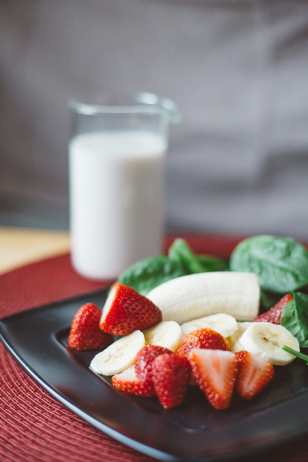 sliced strawberries and bananas on black plate beside white liquid-filled clear drinking glass