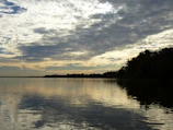 A horizontal panoramic of a serene lake reflecting a cloudy sky.