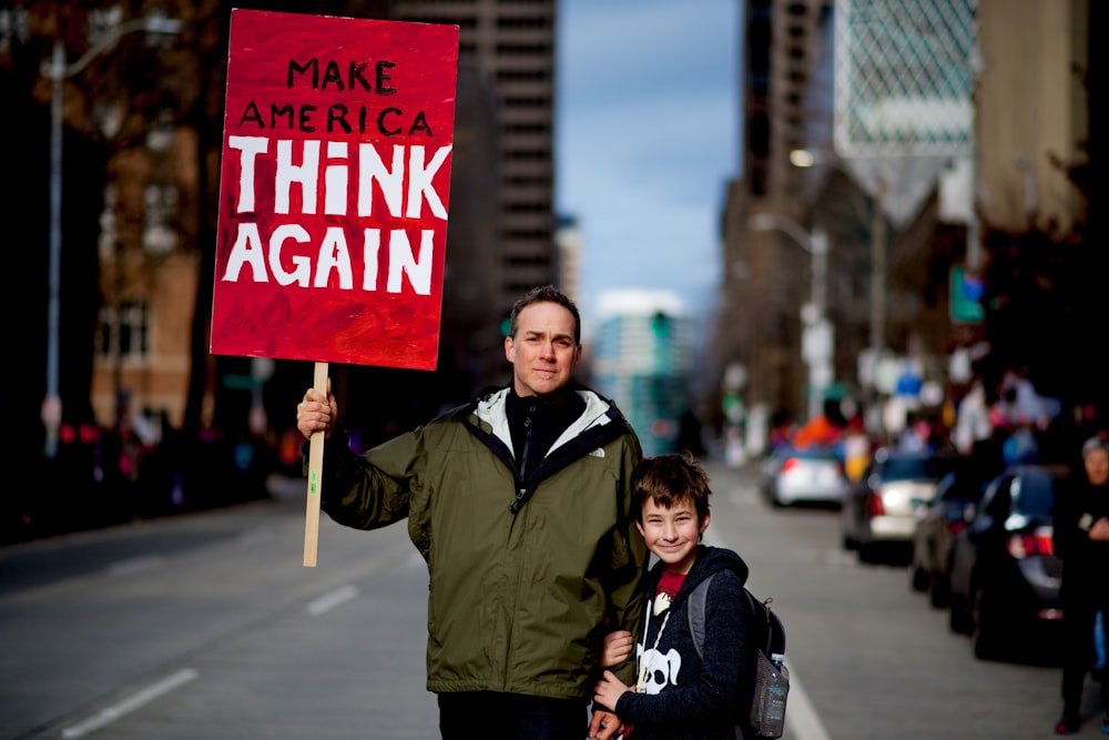 man beside boy holding red and white rally signage