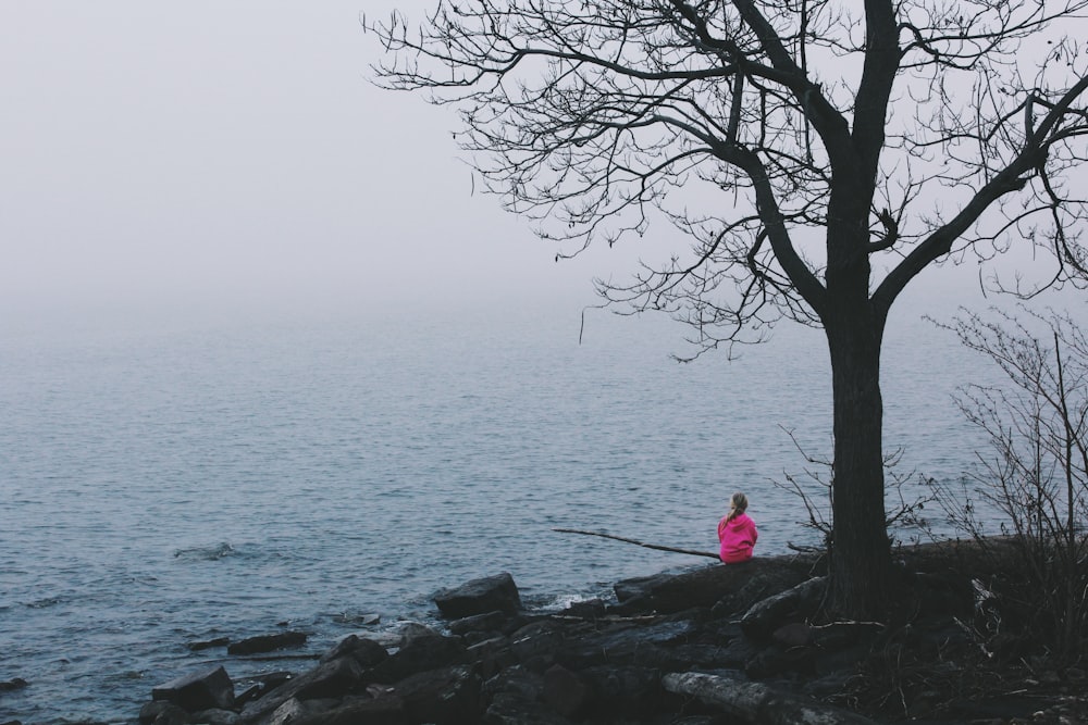 Person in rosa Kleid sitzt in der Nähe des Ozeans