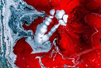An abstract image featuring a vivid interplay of red and silver colors. The design includes swirling patterns and amorphous shapes, with a notable central white-silver structure that stands out prominently against the red background. The composition appears fluid and dynamic, with intricate details and textures.