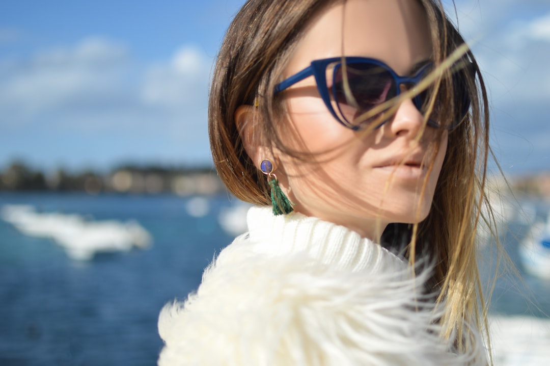 woman wearing blue-framed cat-eye sunglasses with body of water background