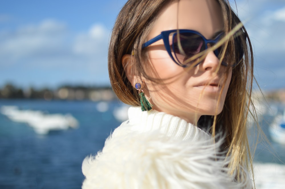 woman wearing blue-framed cat-eye sunglasses with body of water background