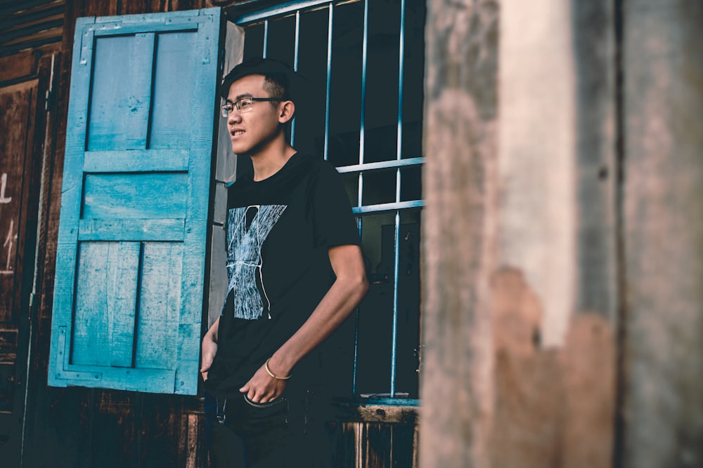 man wearing black crew-neck shirt near blue wooden window