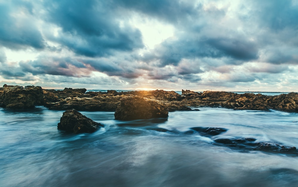 macro photography of water flows at rock formations under nimbus clouds