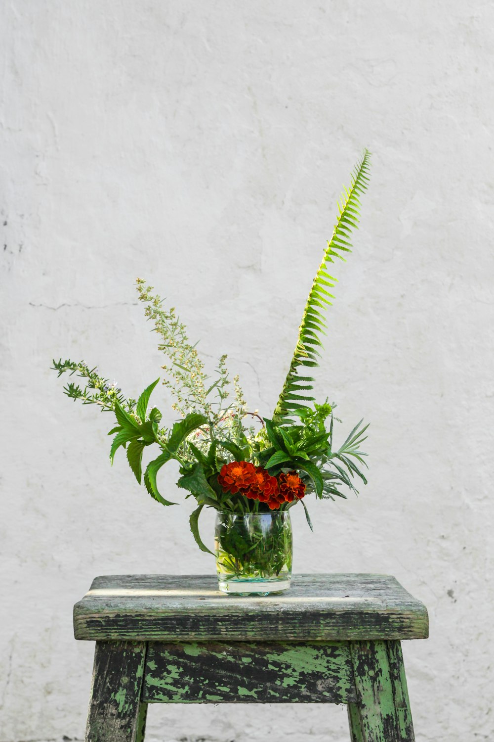 red petaled flowers in glass vase on blue wooden bar stool