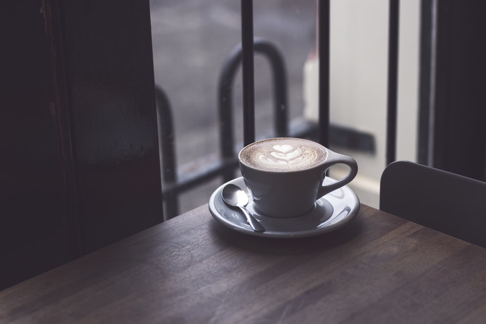 Cappuccino en taza de té blanca sobre superficie de madera marrón