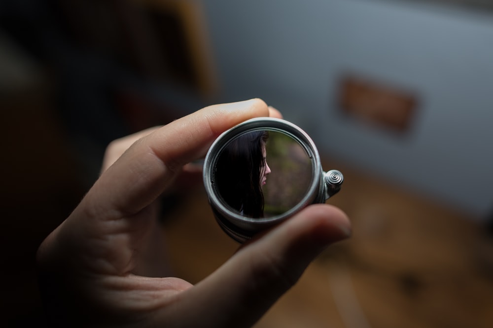 person holding round grey mirror selective focus photography