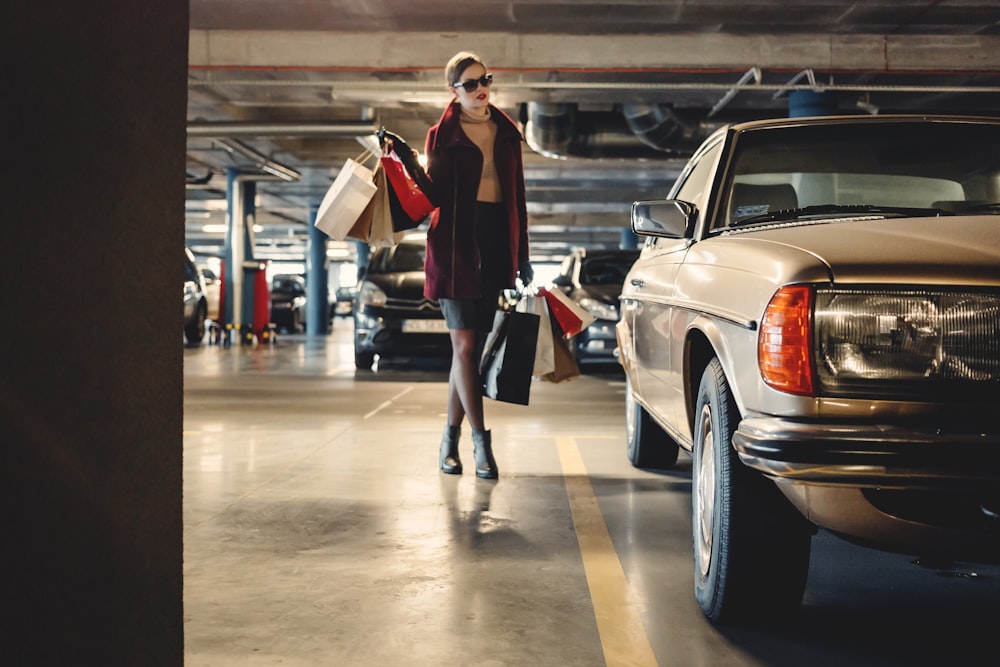 donna che trasporta sacchetti di carta della spesa che cammina verso l'auto beige all'interno del parcheggio