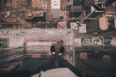 man standing on glass platform on top of building looking down on ground at daytime