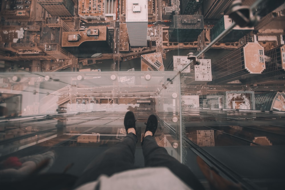 hombre de pie en la plataforma de vidrio en la parte superior del edificio mirando hacia abajo en el suelo durante el día