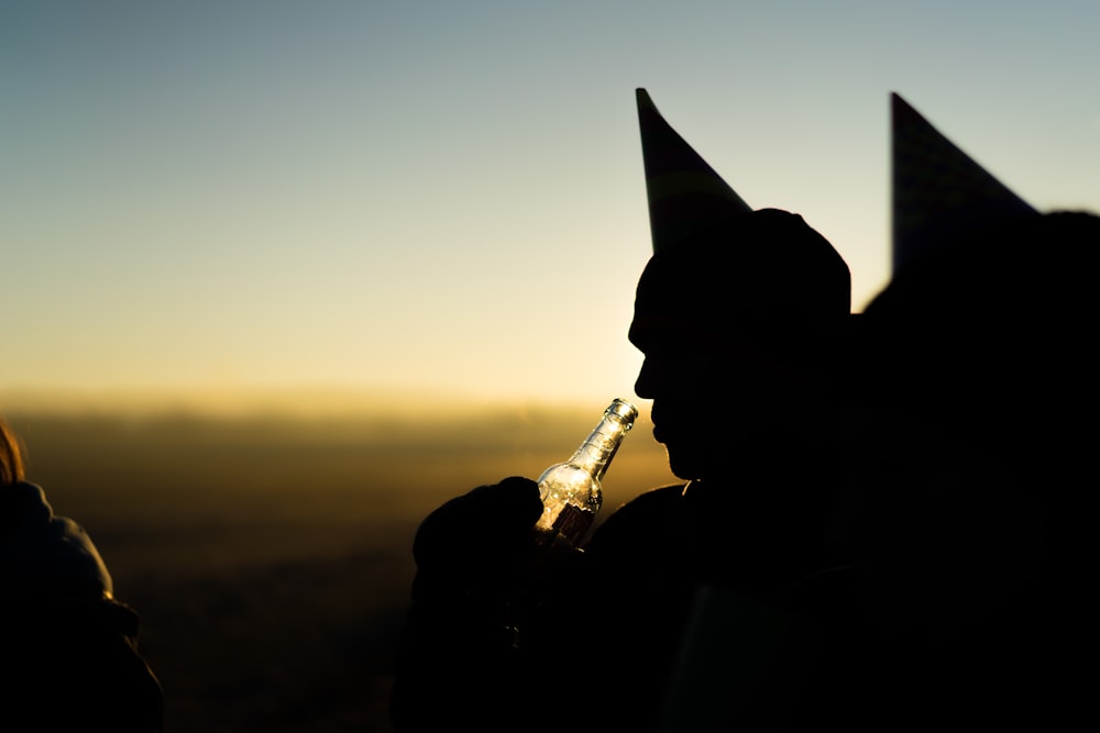 Silueta de la persona que sostiene la botella durante la puesta del sol naranja